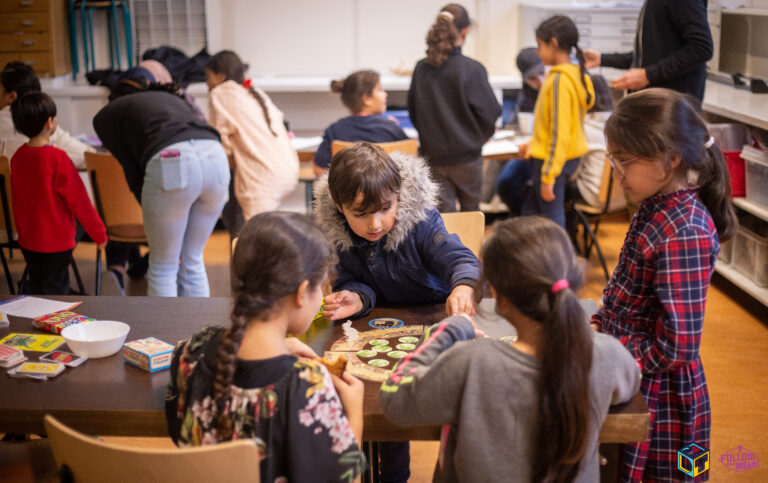 Jonge kinderen zitten aan tafels spelletjes te spelen.