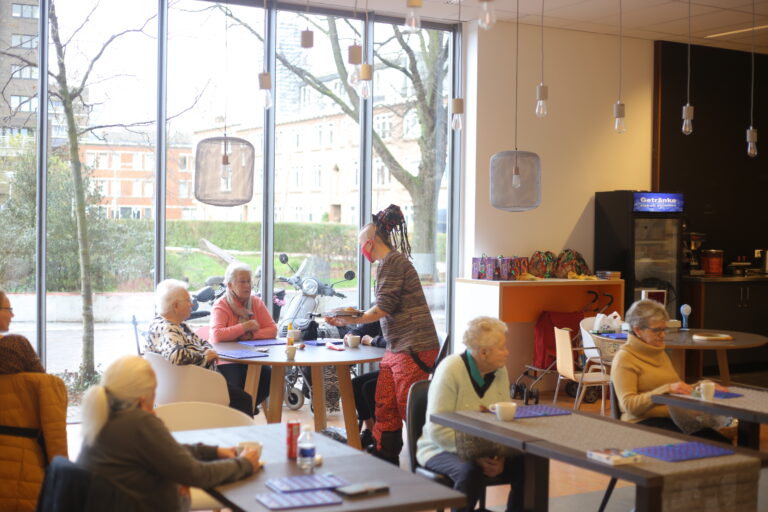 Een vrouw serveert iets aan bejaarden tijdens een bingomiddag.