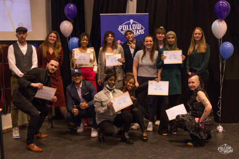 14 jongeren poseren met diploma's in een feestelijke setting.